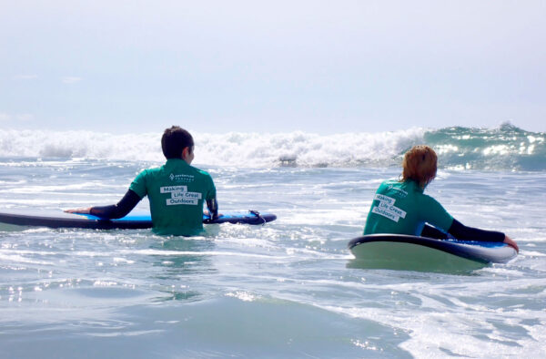 Two young people taking their boards out into the surf